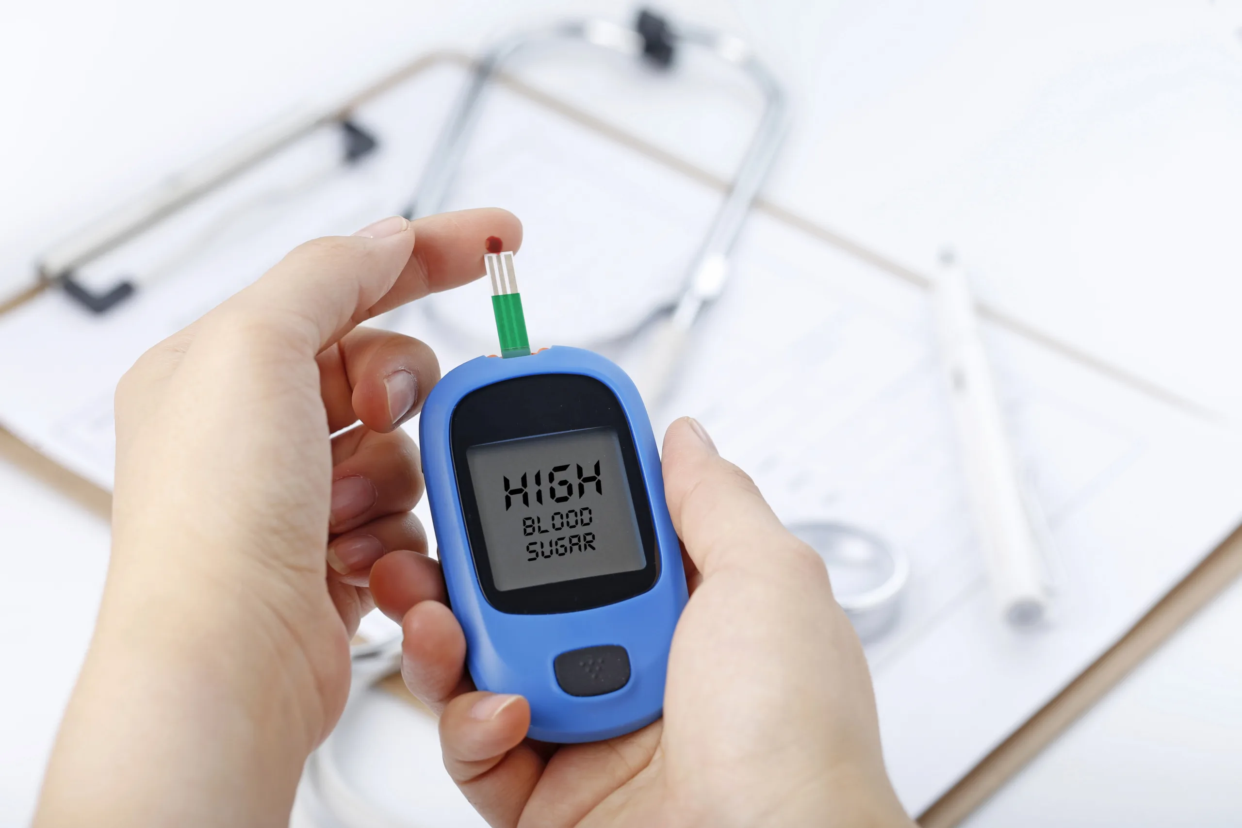 hand holding blood glucose meter measuring blood sugar background is stethoscope chart file scaled