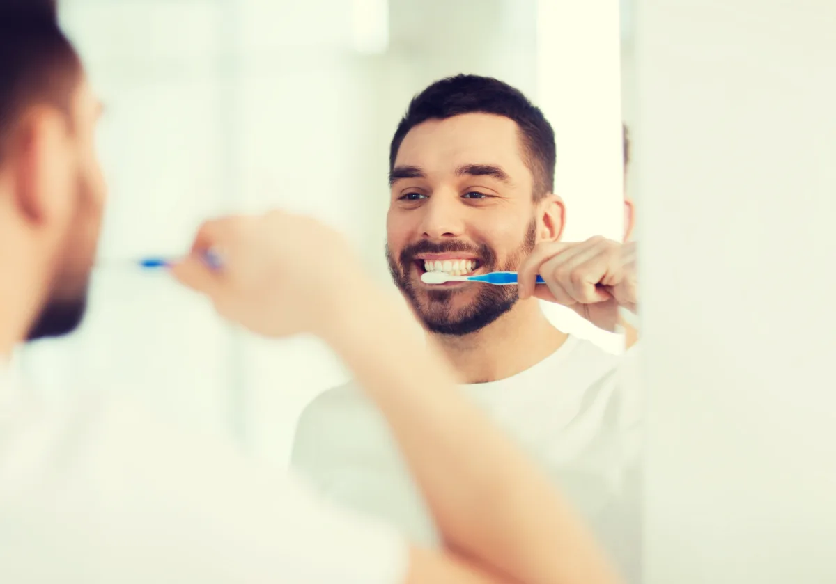 health care dental hygiene people beauty concept smiling young man with toothbrush cleaning teeth looking mirror home bathroom.jpg