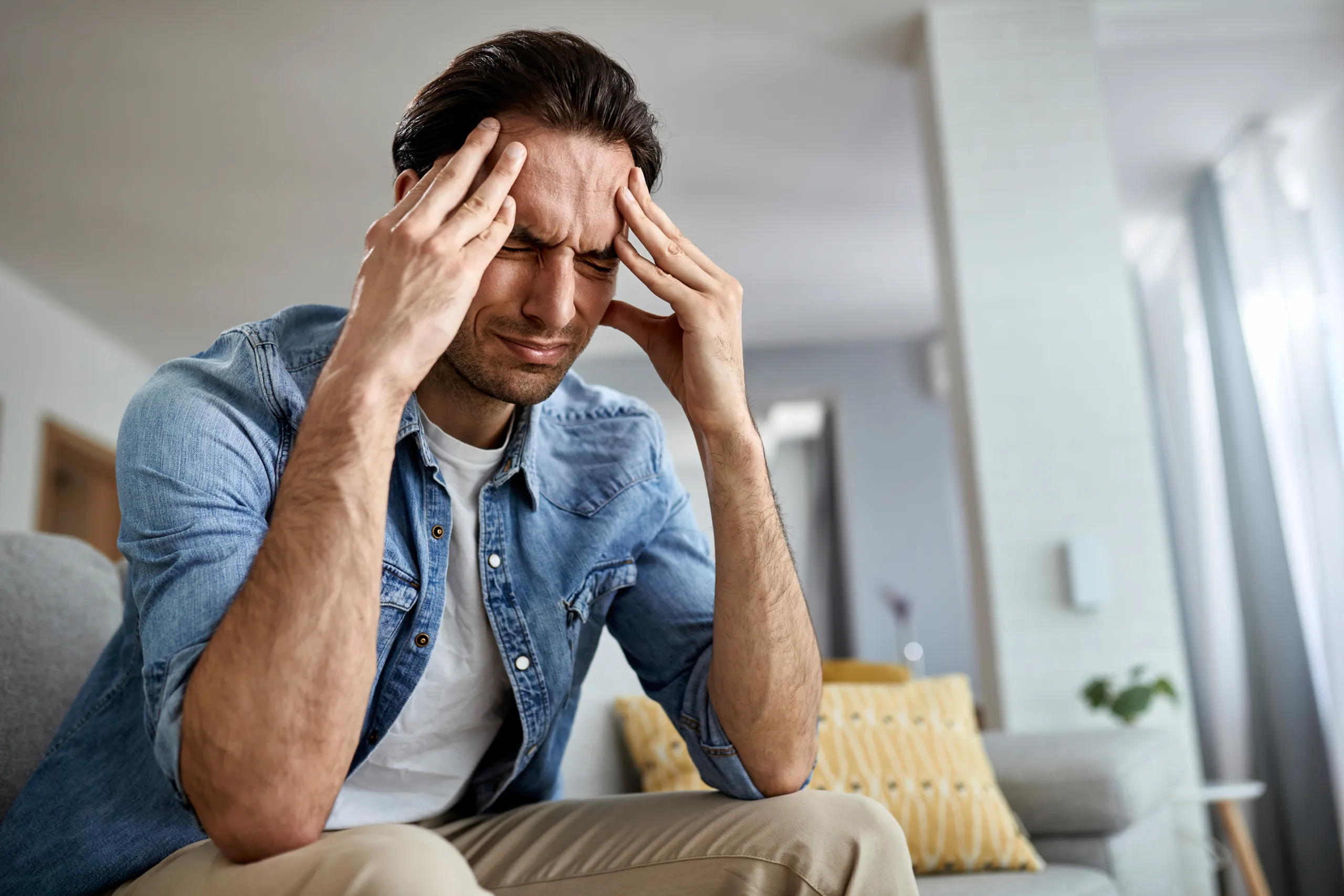 low angle view distraught man holding his head pain while sitting living room scaled