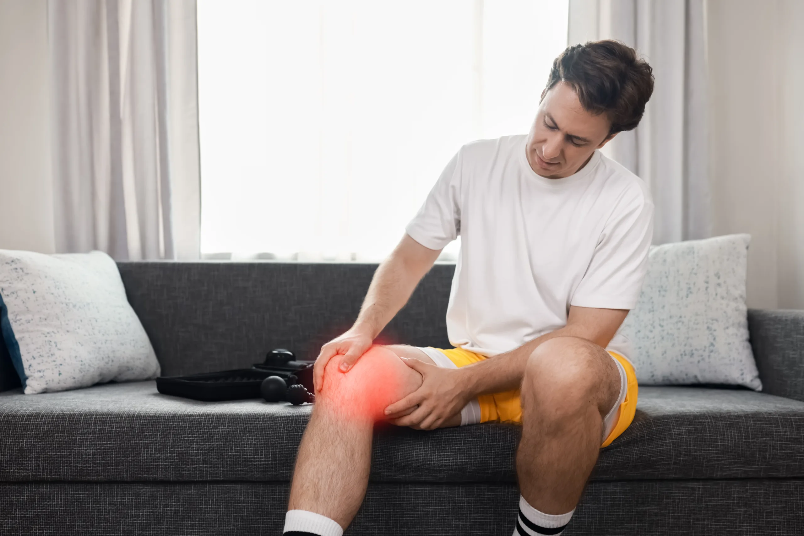 man holds his knee experiencing joint ache pain from sport injury seeking therapy recovery with massager scaled