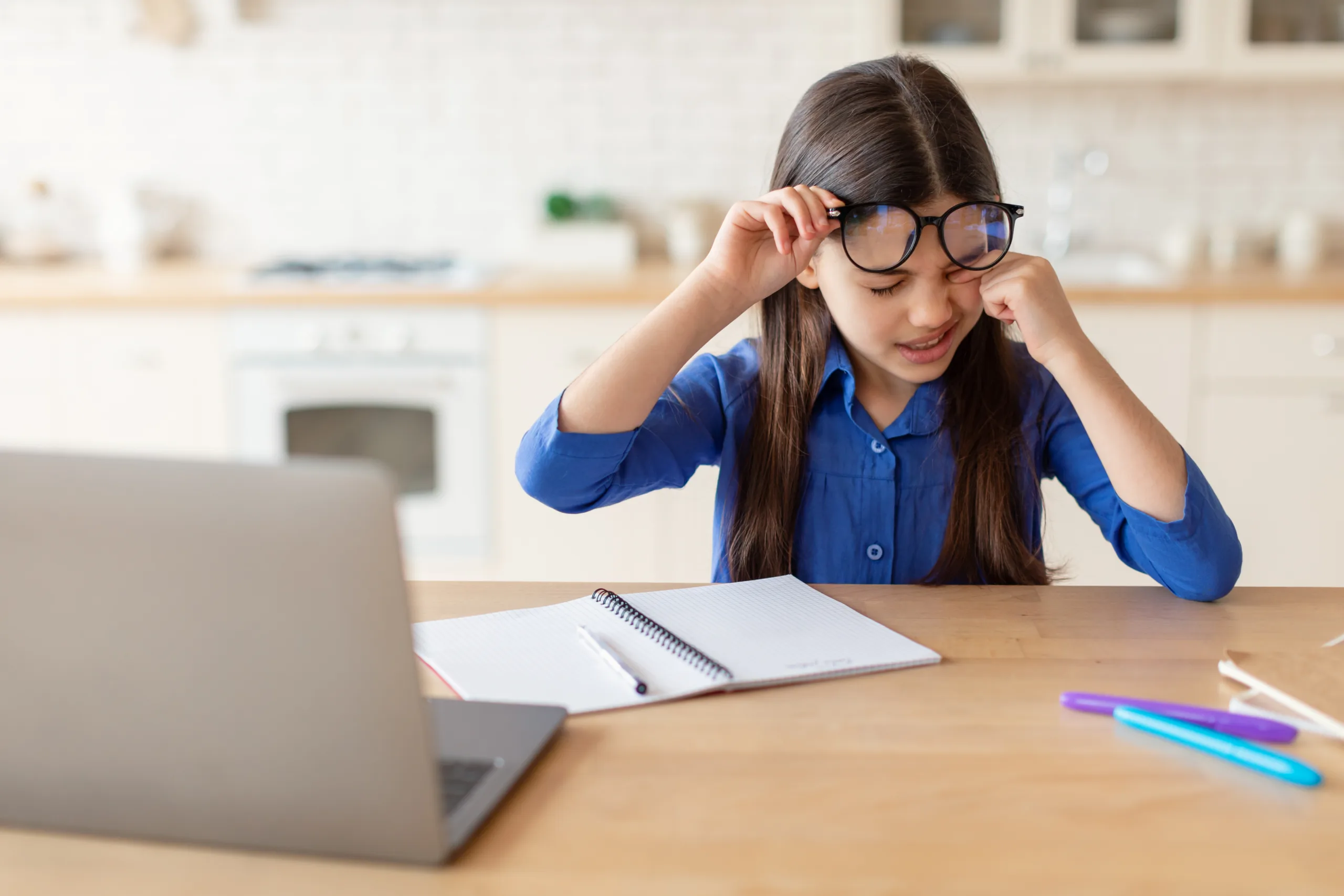 schoolgirl rubbing sore eye using laptop wearing glasses home scaled