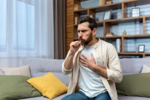 sick mature man alone home sitting sofa coughing holding hands chest living room