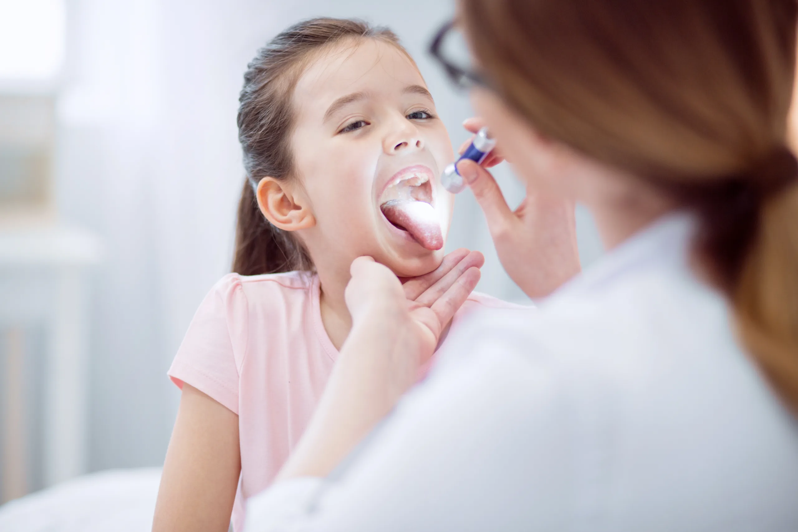 small redness selective focus charming nice little girl opening mouth gazing female doctor who holding flashlight scaled