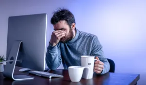tired man sits front computer with cup coffee colored lighting