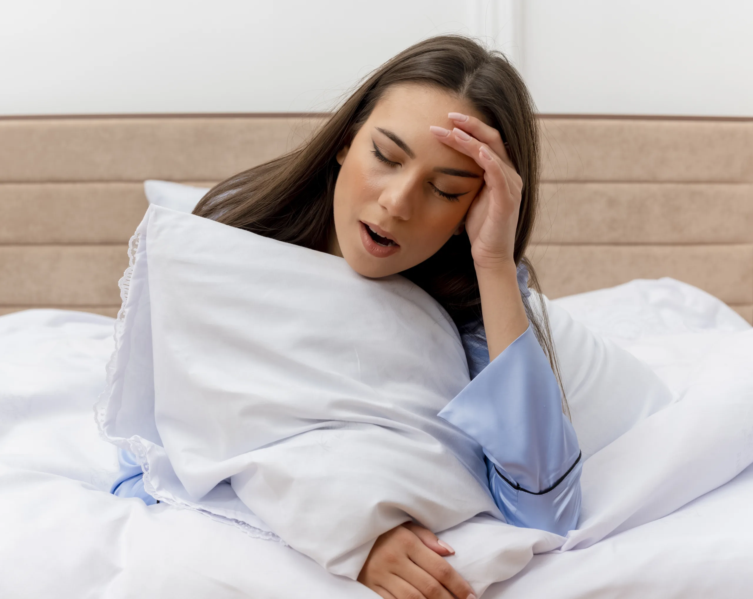 young beautiful woman blue pajamas laying bed with pillow yawning feeling morning fatigue bedroom interior light background scaled